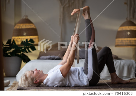 woman working out, warming up using yogic belt, lying in yoga Supta Padangushthasana, One Leg Lift exercise woman working out, warming up using yogic belt, lying in yoga Supta Padangushthasana, One Leg Lift exercise 70416303