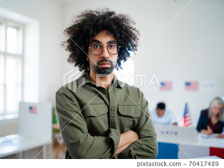 Serious mixed-race man looking at camera in the polling place, usa elections. Serious mixed-race man looking at camera in the polling place, usa elections. 70417489
