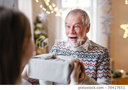 Young woman giving present to surprised grandfather indoors at home at Christmas. 70417651