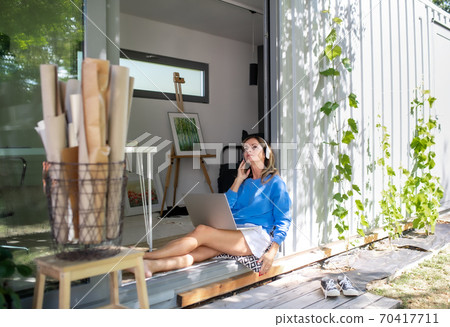 Mature woman working in home office in container house in backyard. Mature woman working in home office in container house in backyard. 70417711