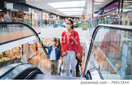 Mother and daughter with face mask on escalator indoors in shopping center, coronavirus concept. Mother and daughter with face mask on escalator indoors in shopping center, coronavirus concept. 70417834