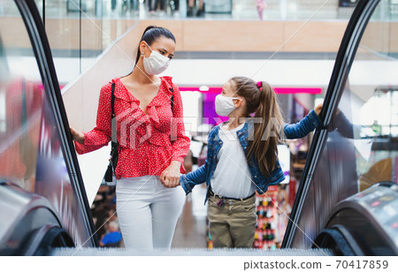 Mother and daughter with face mask on escalator indoors in shopping center, coronavirus concept. Mother and daughter with face mask on escalator indoors in shopping center, coronavirus concept. 70417859