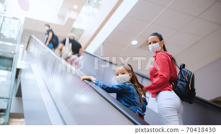 Mother and daughter with face mask on escalator indoors in shopping center, coronavirus concept. Mother and daughter with face mask on escalator indoors in shopping center, coronavirus concept. 70418430