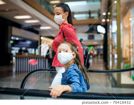 Mother and daughter with face mask on escalator indoors in shopping center, coronavirus concept. Mother and daughter with face mask on escalator indoors in shopping center, coronavirus concept. 70418432