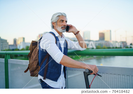 Portrait of mature man with electric scooter outdoors in city, using smartphone. Portrait of mature man with electric scooter outdoors in city, using smartphone. 70418482