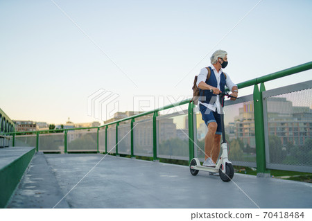 Mature man commuter with face mask and electric scooter outdoors in city, coronavirus concept. Mature man commuter with face mask and electric scooter outdoors in city, coronavirus concept. 70418484