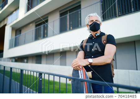 Mature man commuter with face mask and skateboard outdoors in city, coronavirus concept. Mature man commuter with face mask and skateboard outdoors in city, coronavirus concept. 70418485