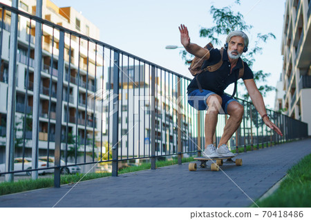 Portrait of mature man riding skateboard outdoors in city, going back to work. Portrait of mature man riding skateboard outdoors in city, going back to work. 70418486