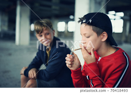 Group of teenagers boys indoors in abandoned building, smoking cigarettes. Group of teenagers boys indoors in abandoned building, smoking cigarettes. 70418493