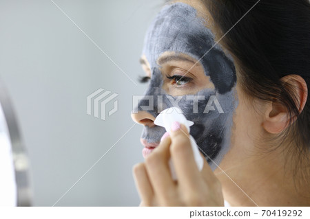 Young woman washes away black clay mask from face portrait Young woman washes away black clay mask from face portrait 70419292