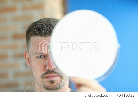 Young man with remnants of hair paste on head stands with mirror in hands portrait 70419332