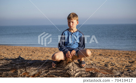 Portrait of a boy. A child is sitting on a log lying on the beach. Portrait of a boy. A child is sitting on a log lying on the beach. 70419417