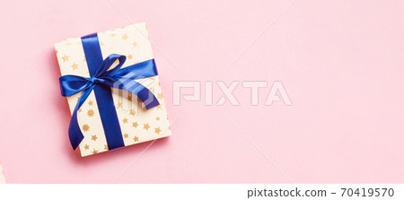 wrapped Christmas or other holiday handmade present in paper with blue ribbon on pink background. Present box, decoration of gift on colored table, top view with copy space 70419570