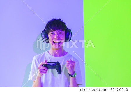 [Image of e-sports] A male gamer who is excited with a controller under purple and green lighting 70420940