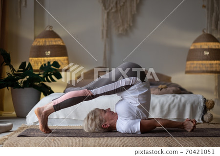 Senior woman practicing yoga, stretching in Plough exercise, Halasana pose, working out Senior woman practicing yoga, stretching in Plough exercise, Halasana pose, working out 70421051