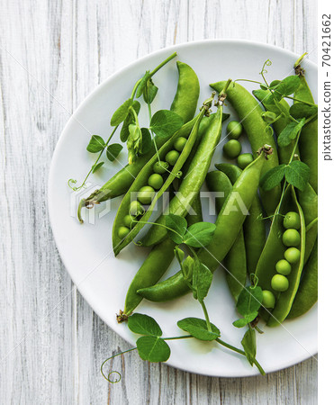 Green peas in a plate on a white wooden background. View from above. Green peas in a plate on a white wooden background. View from above. 70421662
