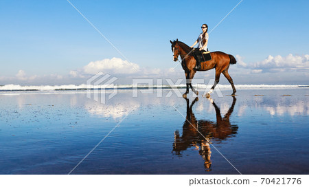 Woman riding horse on beach along sea by water pool. Woman riding horse on beach along sea by water pool. 70421776