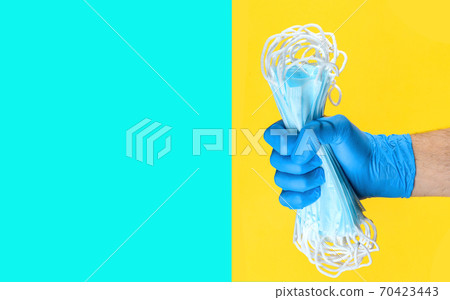 Hand in medical latex gloves holding heap of face protective masks on yellow background. Copy space Hand in medical latex gloves holding heap of face protective masks on yellow background. Copy space 70423443