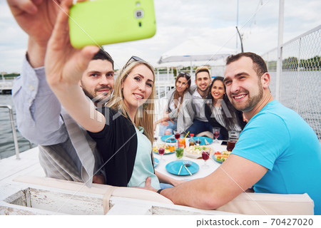 Happy young friends were sitting at a table and having a picnic outdoors. 70427020
