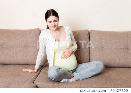 Pregnant woman with painful belly on sofa at home Pregnant woman with painful belly on sofa at home 70427769