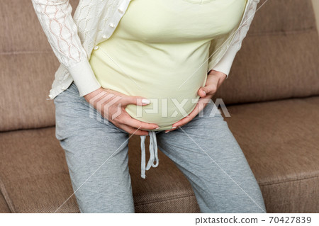Pregnant woman with painful belly on sofa at home 70427839