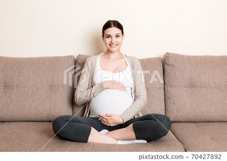 photo of cute caucasian future mom lying in light living room on sofa and holding hands on tummy photo of cute caucasian future mom lying in light living room on sofa and holding hands on tummy 70427892