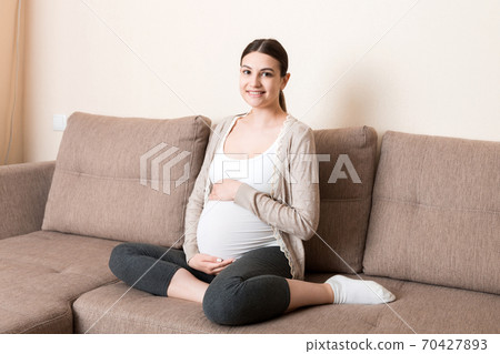 photo of cute caucasian future mom lying in light living room on sofa and holding hands on tummy photo of cute caucasian future mom lying in light living room on sofa and holding hands on tummy 70427893