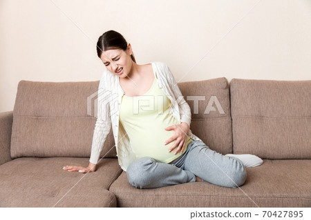 Pregnant woman with painful belly on sofa at home Pregnant woman with painful belly on sofa at home 70427895