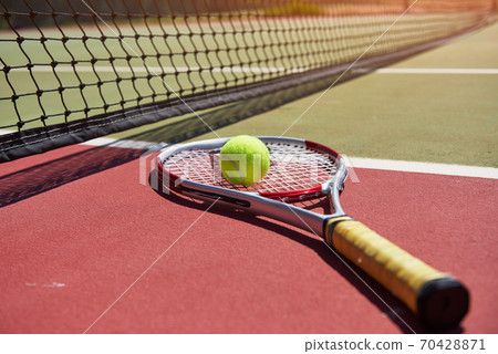 A tennis racket and new tennis ball on a freshly painted tennis court. 70428871