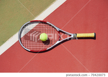 A tennis racket and new tennis ball on a freshly painted tennis court. 70428873