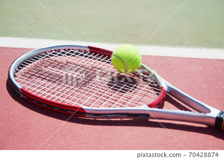 A tennis racket and new tennis ball on a freshly painted tennis court. 70428874