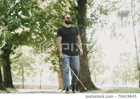 Blind young man in black sunglasses walking outdoors Blind young man in black sunglasses walking outdoors 70429645