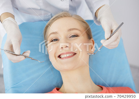 Smiling caucasian woman is being examined by dentist at dental clinic. Healthy teeth and medicine, stomatology concept Smiling caucasian woman is being examined by dentist at dental clinic. Healthy teeth and medicine, stomatology concept 70429950