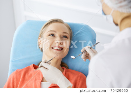 Smiling caucasian woman is being examined by dentist at dental clinic. Healthy teeth and medicine, stomatology concept Smiling caucasian woman is being examined by dentist at dental clinic. Healthy teeth and medicine, stomatology concept 70429960
