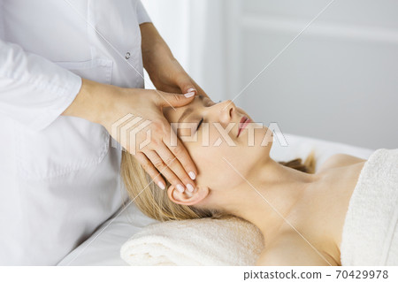 Beautiful caucasian woman enjoying facial massage with closed eyes in spa salon. Relaxing treatment in medicine and Beauty concept 70429978