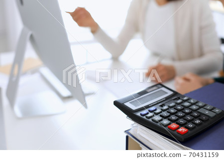 Calculator and binders with papers are waiting to be processed by business woman or bookkeeper working at the desk in office back in blur. Internal Audit and tax concept 70431159