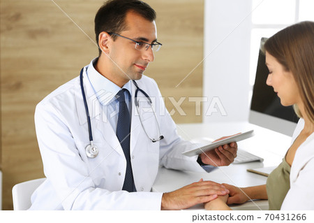 Doctor reassuring her female patient because of her first pregnancy fear while sitting at a desk in a clinic. Concept of comforting, empathy and best medical service Doctor reassuring her female patient because of her first pregnancy fear while sitting at a desk in a clinic. Concept of comforting, empathy and best medical service 70431266