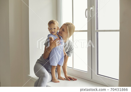 Cute toddler boy and young mommy relaxing on windowsill of big window in new home 70431866