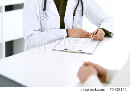 Woman doctor and patient sitting and talking at medical examination at hospital office, close-up. Therapist filling up medication history records. Medicine and healthcare concept 70432131