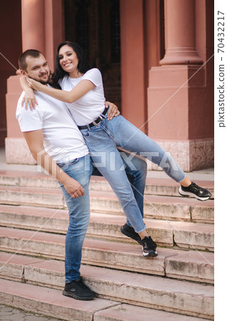 Two belowed people walking in the city. Beautiful couple in denim and white t-shirt have fun Two belowed people walking in the city. Beautiful couple in denim and white t-shirt have fun 70432217