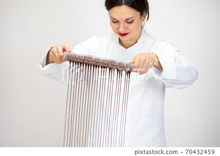 Attractive Female chocolatier pouring excess melted dark chocolate from molds 70432459