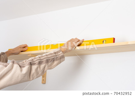 A man hangs a shelf in an apartment A man hangs a shelf in an apartment 70432952