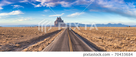 Panoramic View of a road in a dry desert with Shiprock 70433684