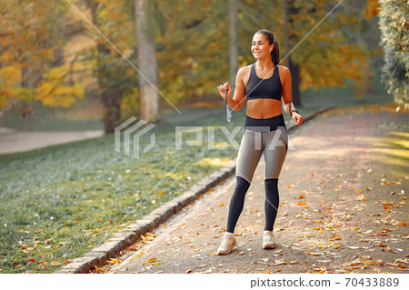 Sports girl in a black top training in a autumn park 70433889
