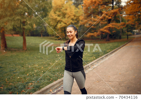 Sports girl in a black top training in a autumn park 70434116