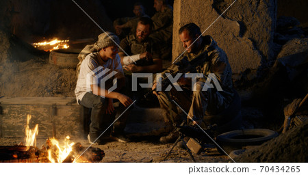 Soldier showing gun to ethnic teenager near campfire 70434265