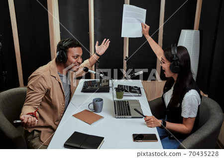 Portait of two radio hosts, young man and woman looking emotional while talking with each other, moderating a live show in studio 70435228