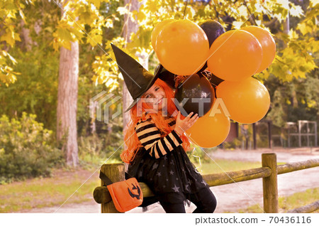 A child in a carnival costume on Halloween with large colored balloons. Little girl in the autumn A child in a carnival costume on Halloween with large colored balloons. Little girl in the autumn 70436116