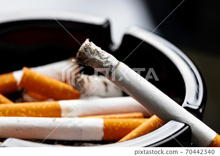 Burning cigarette in a black ash tray 70442340