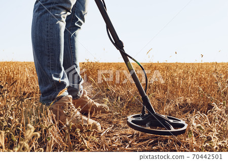 Man with metal detector equipment searching for metal goods in the field 70442501
